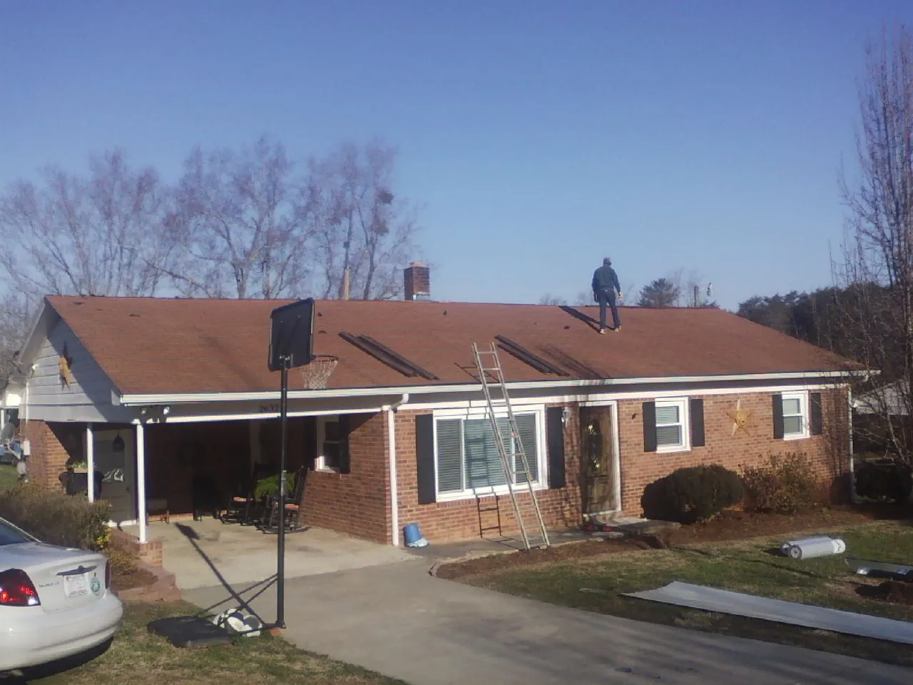 Roofer stripping a shingle roof on a brick ranch before metal panels in Lamont