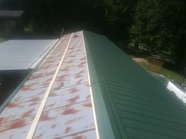 Old rusted panels beside newly installed green metal roofing — Wind Damage Roof Repair by Roofing Brothers in Lamont